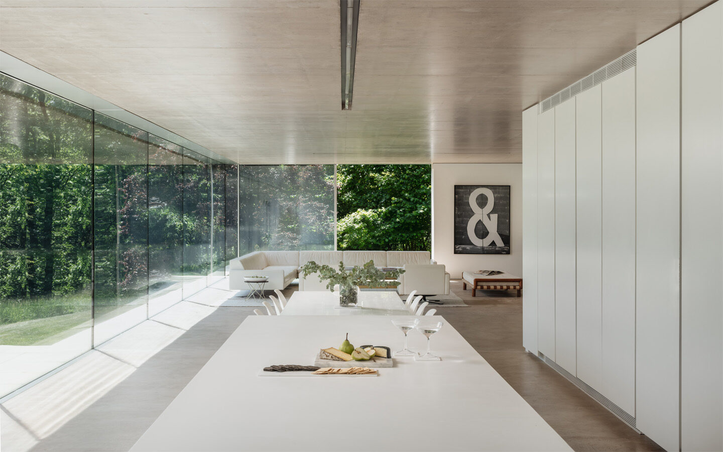 Modern minimalist living room with glass walls and greenery.