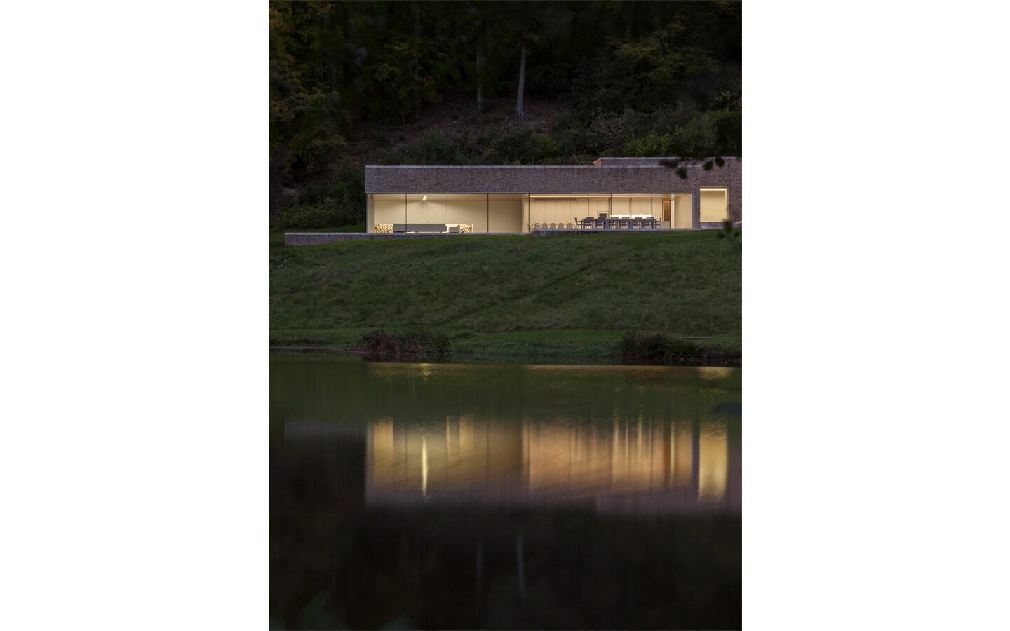Modern lakeside house with large windows at dusk.