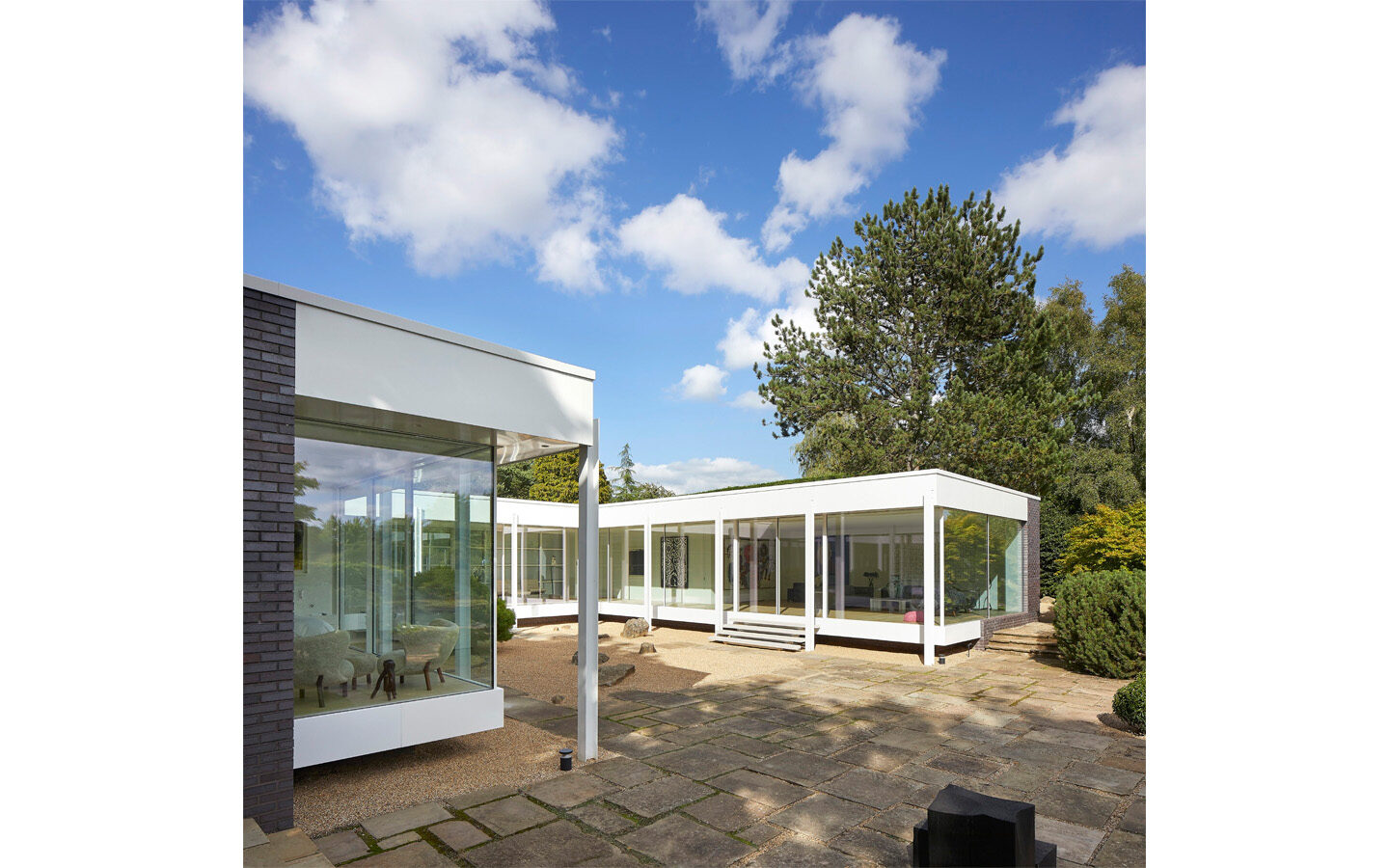 Modern glass house with large trees and blue sky.